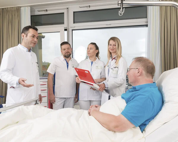 Visite, © Krebsinformationsdienst, DKFZ; Foto: Tobias Schwerdt Arzte und Ärztinnen stehen vor einem Patenten, der im Bett liegt, und halten Visite.