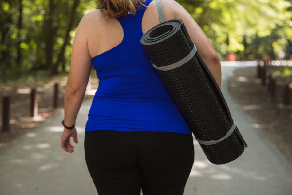 Eine etwas übergewichtige Frau trägt eine Trainingsmatte, von hinten fotografiert