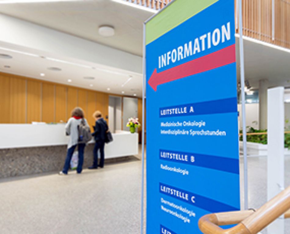 Eingangsbereich Krankenhaus mit Informationstafel und Patientinnen © Krebsinformationsdienst, Deutsches Krebsforschungszentrum