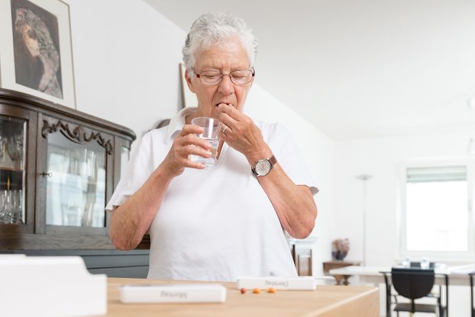 Ältere Dame nimmt Medikamente mit einem Glas Wasser ein.