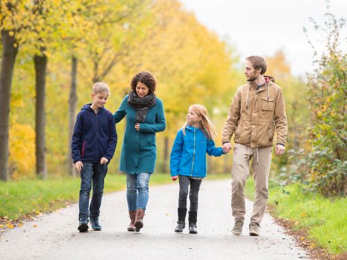 Mutter und Vater gehen mit ihren zwei Kindern im herbstlichen Park spazieren und sprechen intensiv miteinander.