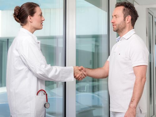Eine Ärztin (links) und ein Arzt (rechts) schütteln sich die Hände.