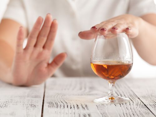 Ein Frau lehnt mit der Hand ein Glas Alkohol ab. 