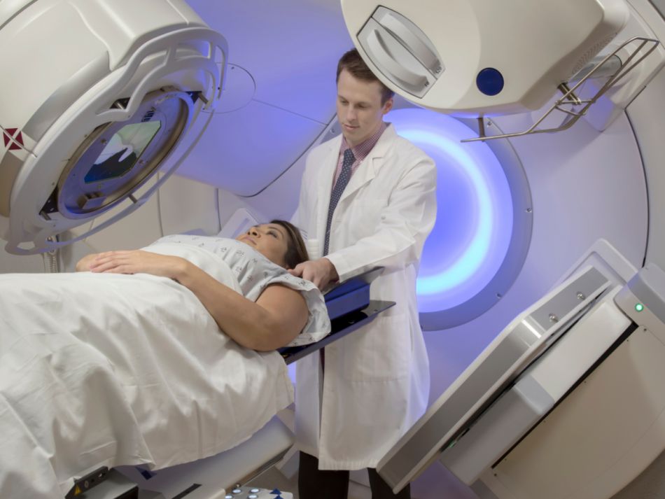 Ein junger Arzt steht hinter einer junge Frau, die auf dem Untersuchungstisch des Bestrahlungsgerätes liegt.