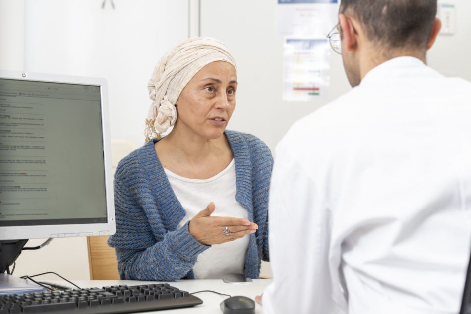 Krebspatientin mit Kopftuch spricht mit ihrem Arzt im Arztzimmer.