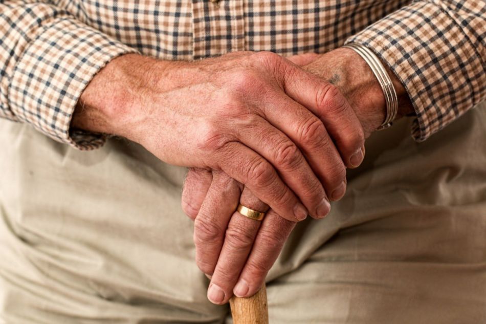 Bildausschnitt: gefaltete Hände eines alten Mannes auf seinem Gehstock.