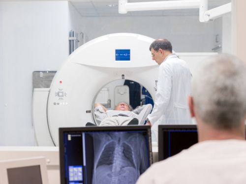 Ein Lungenkrebspatient liegt in einem MRT-Gerät. Ein Arzt ist mit im Raum. Im Vordergrund sieht man ein MRT-Bild der Lunge im Überwachungsraum.