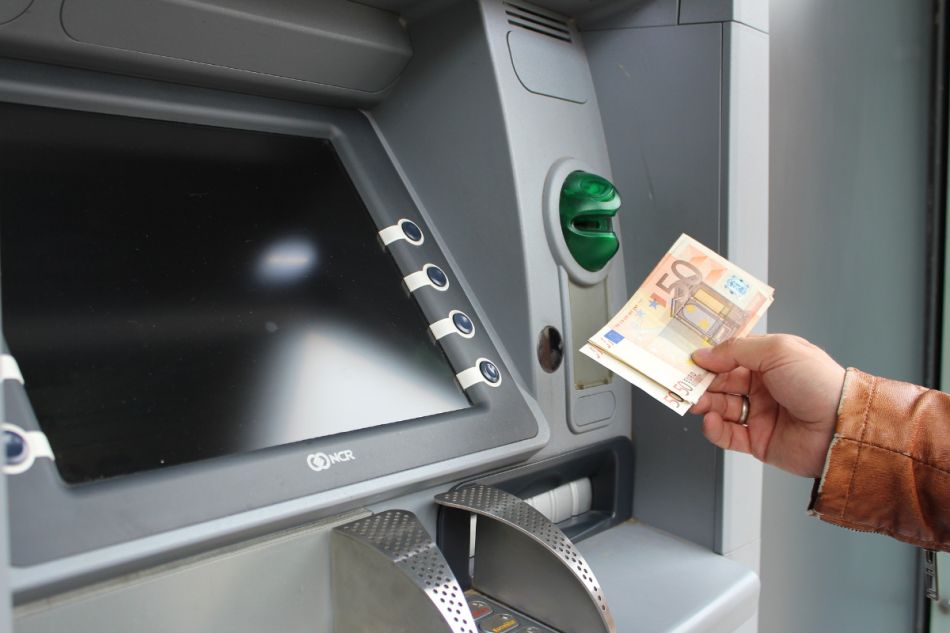 Eine Hand hält 50 Euro vor den Ausgabeschlitz eines Geldautomaten