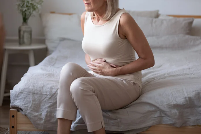Unterleibsschmerzen, © fizkes, Shutterstock Eine Frau sitzt auf der Bettkante und hält sich schmerzerfüllt den Bauch