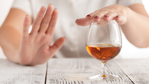 Ein Frau lehnt mit der Hand ein Glas Alkohol ab.