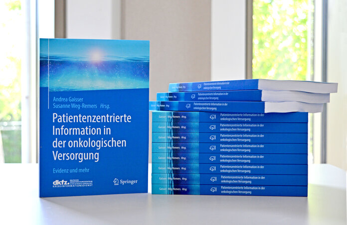 Cover und Stapel des blauen KID-Buchs "Patientenzentrierte Information in der onkologischen Versorgung"