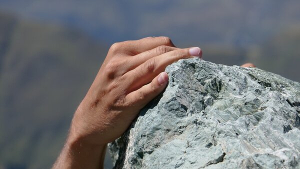 Hände halten sich an Fels fest.