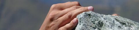 Hände halten sich an Fels fest.