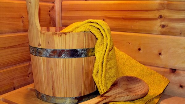 Wassereimer aus Holz, Holzschöpflöffel und gelbes Handtuch in einer Holzsauna.