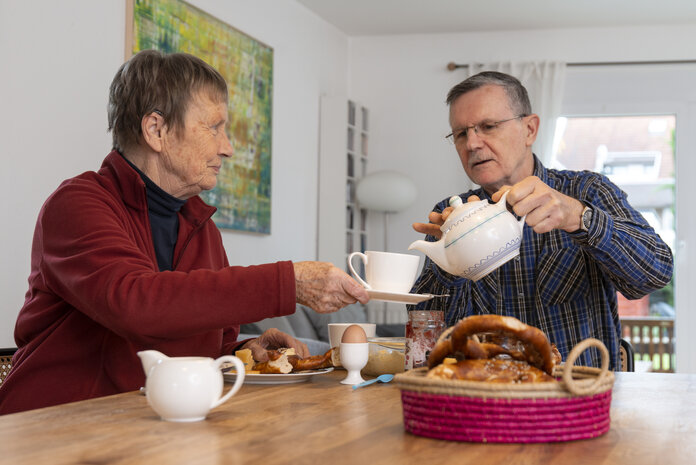 Älterer Herr schenkt einer älteren Dame am Frühstückstisch Tee ein.