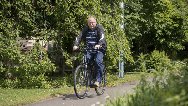 Ein Herr fährt mit dem Fahrrad auf einem Fahrradweg durch die Natur