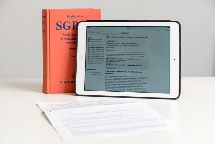 Das Sozialgesetzbuch steht auf einem Tisch, daneben ein Tablet und ein Dokument.