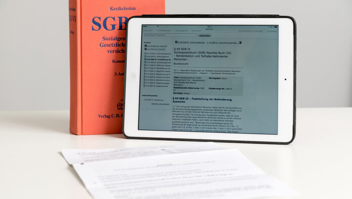 Das Sozialgesetzbuch steht auf einem Tisch, daneben ein Tablet und ein Dokument.