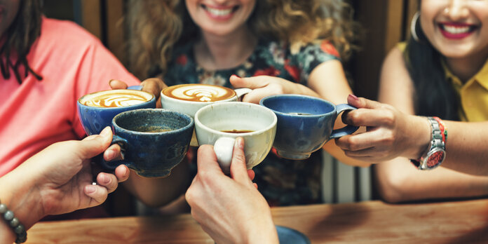 Eine Gruppe junger Menschen stößt mit Kaffeetassen an.