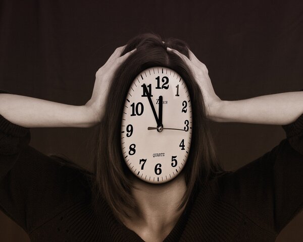 Frau, deren Gesicht durch das Ziffernblatt einer Uhr ersetzt ist, greift sich verzweifelt an den Kopf.