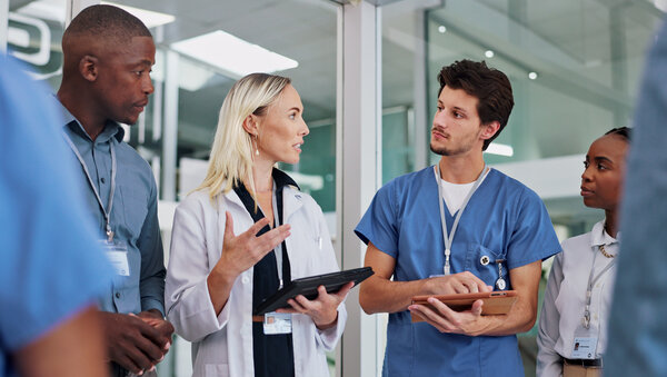 Ambulante spezialfachärztliche Versorgung, © The Yuri Arcurs Collection, Freepik Eine Gruppe Ärztinnen und Ärzte steht beieinander, eine Frau hebt ein Tablet und spricht in die Runde.