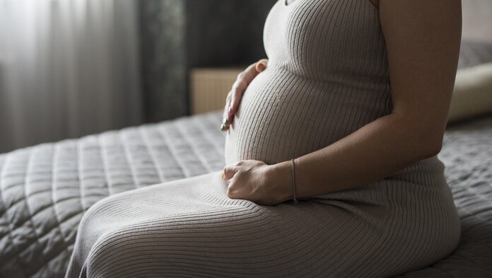 Eine schwangere Frau sitzt auf einem Bett und hält ihren Bauch.