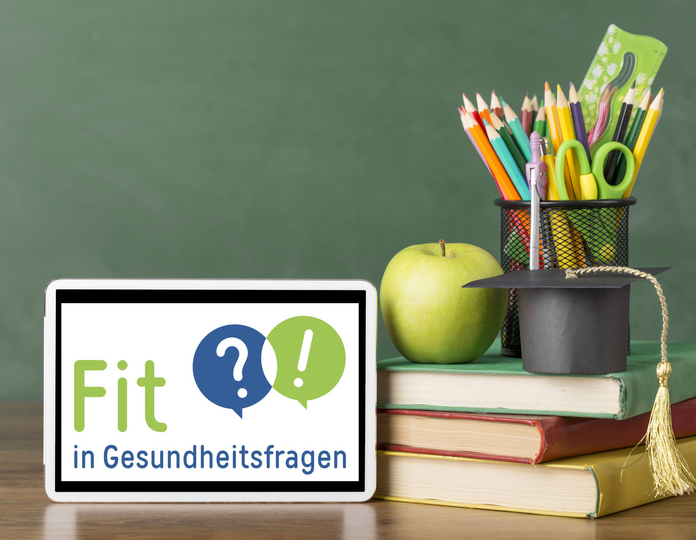 Das Logo des Projekts "Fit in Gesundheitsfragen" ist auf einem Tisch neben einem Bücherstapel, einem Apfel und Stiften abgebildet.