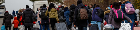 Eine Gruppe ukrainischer Flüchtlinge mit Gepäck und Rollkoffern geht eine Straße entlang