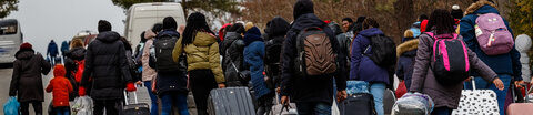Eine Gruppe ukrainischer Flüchtlinge mit Gepäck und Rollkoffern geht eine Straße entlang