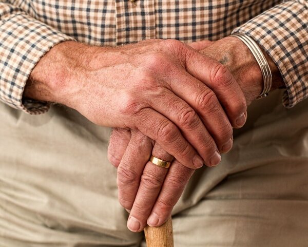 Bildausschnitt: gefaltete Hände eines alten Mannes auf seinem Gehstock.