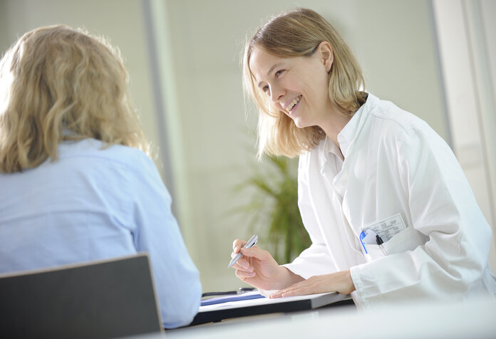 Ärztin am Schreibtisch führt ein freundliches Gespräch mit einer Patientin.