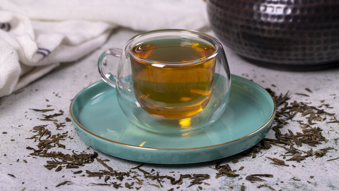 Eine Tasse mit grünem Tee. Darum liegen Teeblätter.