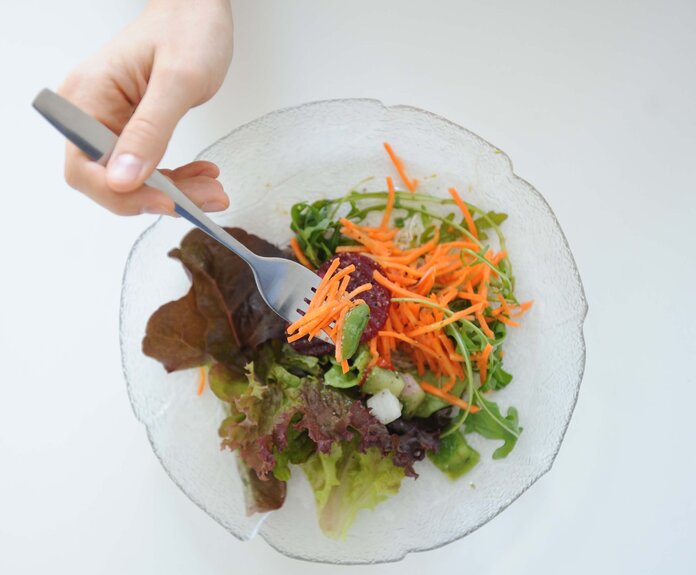 Eine Hand piekt mit einer Gabel in einen gemischten Salat