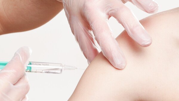 Spritze mit einer Impfung wird an den Arm gehalten