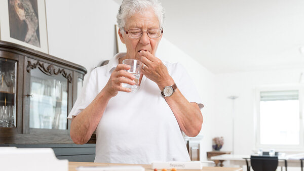 Ältere Dame nimmt Medikamente mit einem Glas Wasser ein.