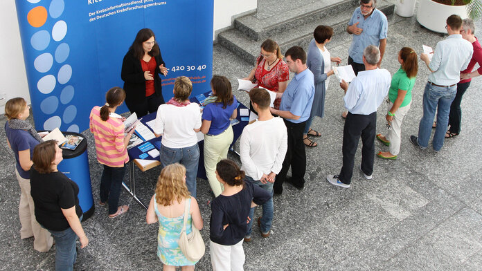 Eine Besuchergruppe mit rund 15 Personen ist im Gespräch an einem Informationsstand des Krebsinformationsdienstes.