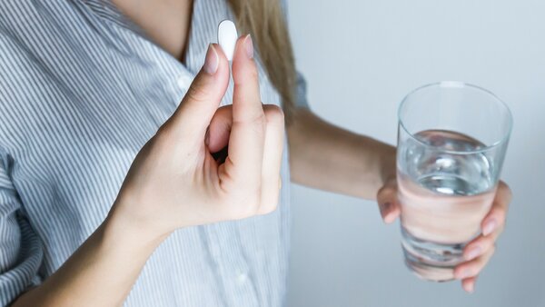 Frau nimmt eine Tablette ein mit einem Glas Wasser.