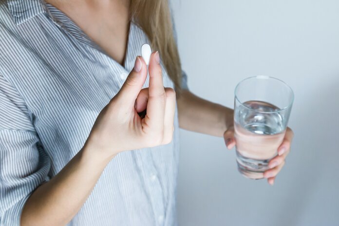 Frau nimmt eine Tablette ein mit einem Glas Wasser.