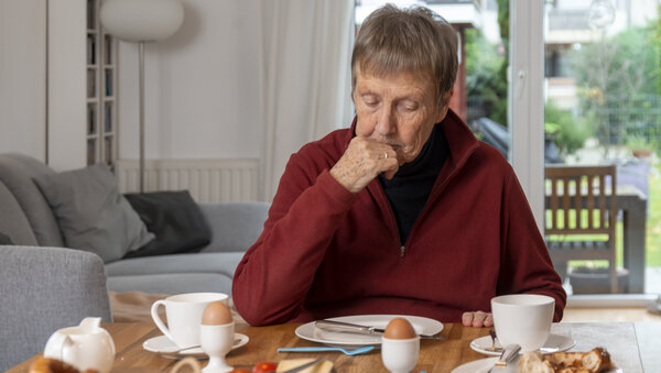 Eine ältere Frau sitzt ohne Appetit an einem Esstisch mit Frühstück.