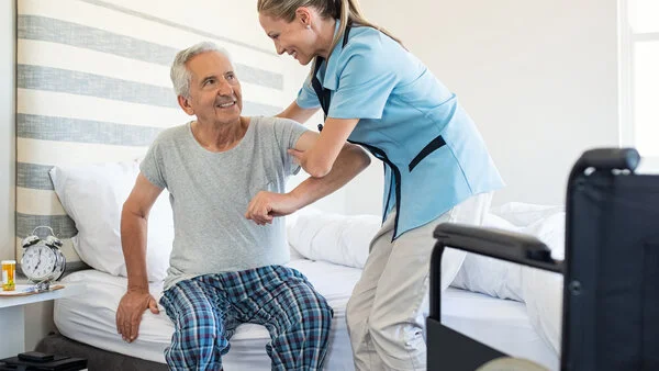 Pflege, © Rido, Shutterstock Eine Pflegerin hilft einem Patienten Zuhause am Bett.