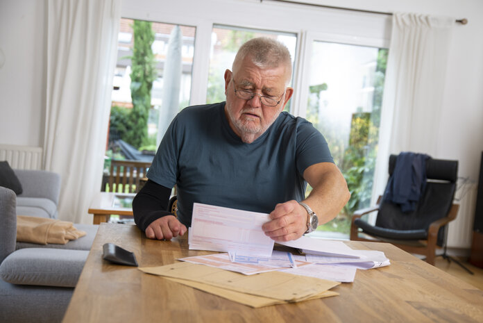 Ein älterer Mann sitzt am Wohnzimmertisch und sortiert medizinische Dokumente.