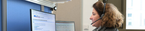 Eine Ärztin vom Telefondienst des Krebsinformationsdienstes sitzt an einem Arbeitsplatz mit 2 Computer-Bildschirmen, auf die sie schaut, während sie über ein Headset telefoniert.