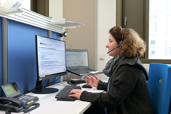 Eine Ärztin vom Telefondienst des Krebsinformationsdienstes sitzt an einem Arbeitsplatz mit 2 Computer-Bildschirmen, auf die sie schaut, während sie über ein Headset telefoniert.