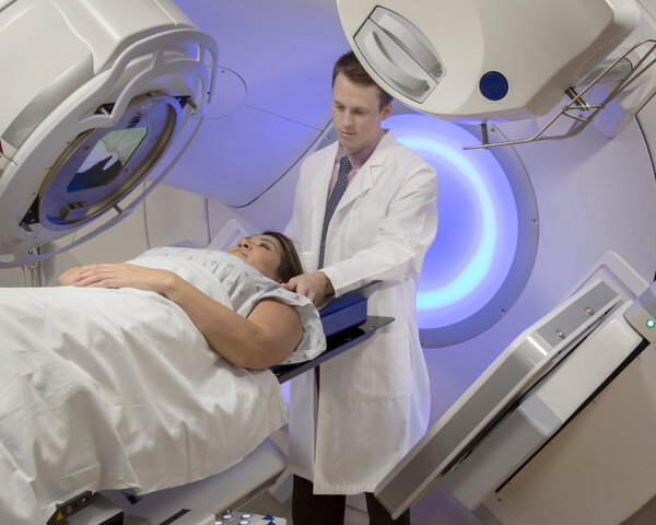 Eine Frau liegt auf einer Liege unter dem Bestrahlungsgerät. Hinter ihr steht ein junger Arzt.