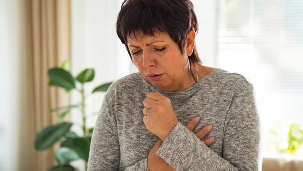 Husten, © Aleksandra Suzi, Shutterstock Eine Frau mit kurzen Haaren hustet in ihre Hand.