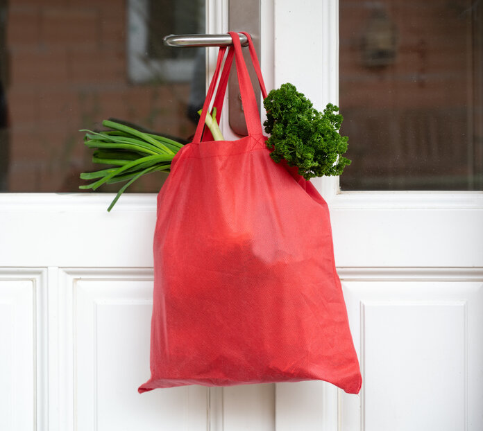 Eine rote Tasche mit Lebensmitteleinkäufen hängt an einer Tür.