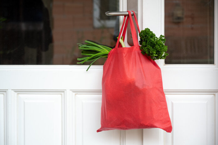 Eine rote Tasche mit Lebensmitteleinkäufen hängt an einer Tür.