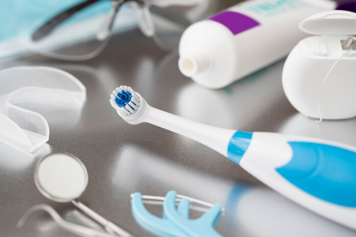 Verschiedene Utensilien für die Zahnpflege bei Krebs liegen auf einem Tisch: elektrische Zahnbürste, Zahnpasta, Zahnseide, Spiegel etc.