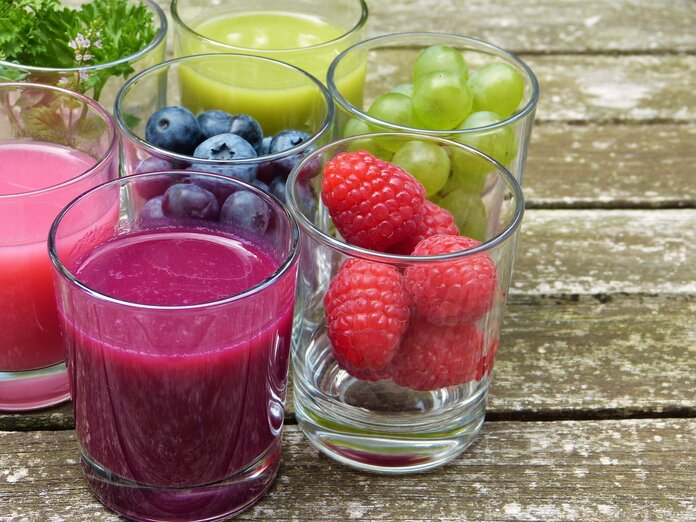 Kleine Gläser mit Himbeeren, Heidelbeeren, Weintrauben sowie bunten Smoothies.