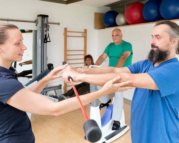 Ein Mann trainiert mit einer Physiotherapeutin in einem Sportraum.